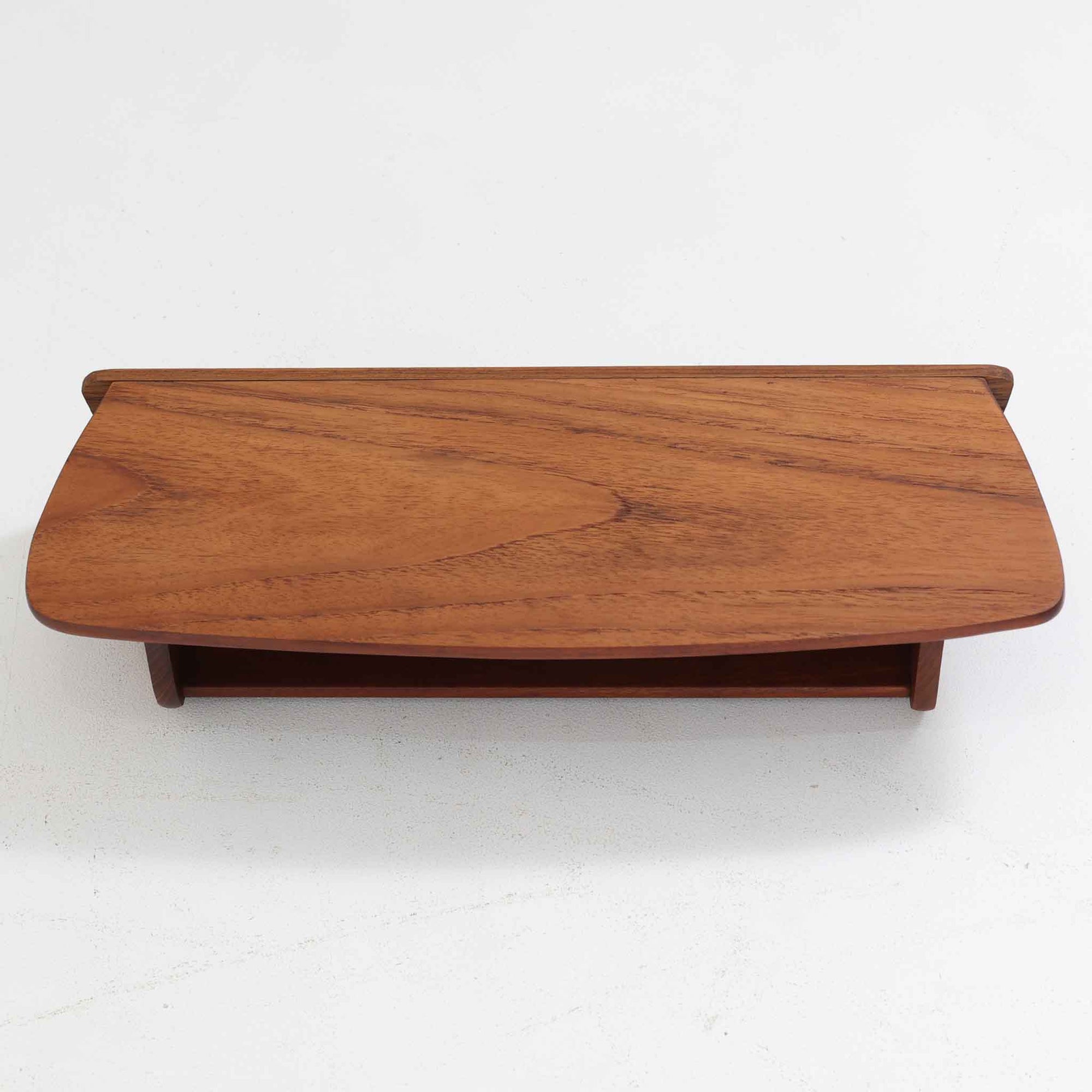 デンマーク製ウォールシェルフです。上質なチーク無垢材を使用し、滑らかなカーブを描く縁取りと丸みのあるフォルムが北欧家具らしい柔らかさを感じさせます。奥行きを抑えたコンパクトなサイズで、玄関や寝室、リビングのちょっとしたスペースにも取り付けやすい設計です。経年により深みを増したチーク材の美しい色合いが、壁面を上品に演出します。