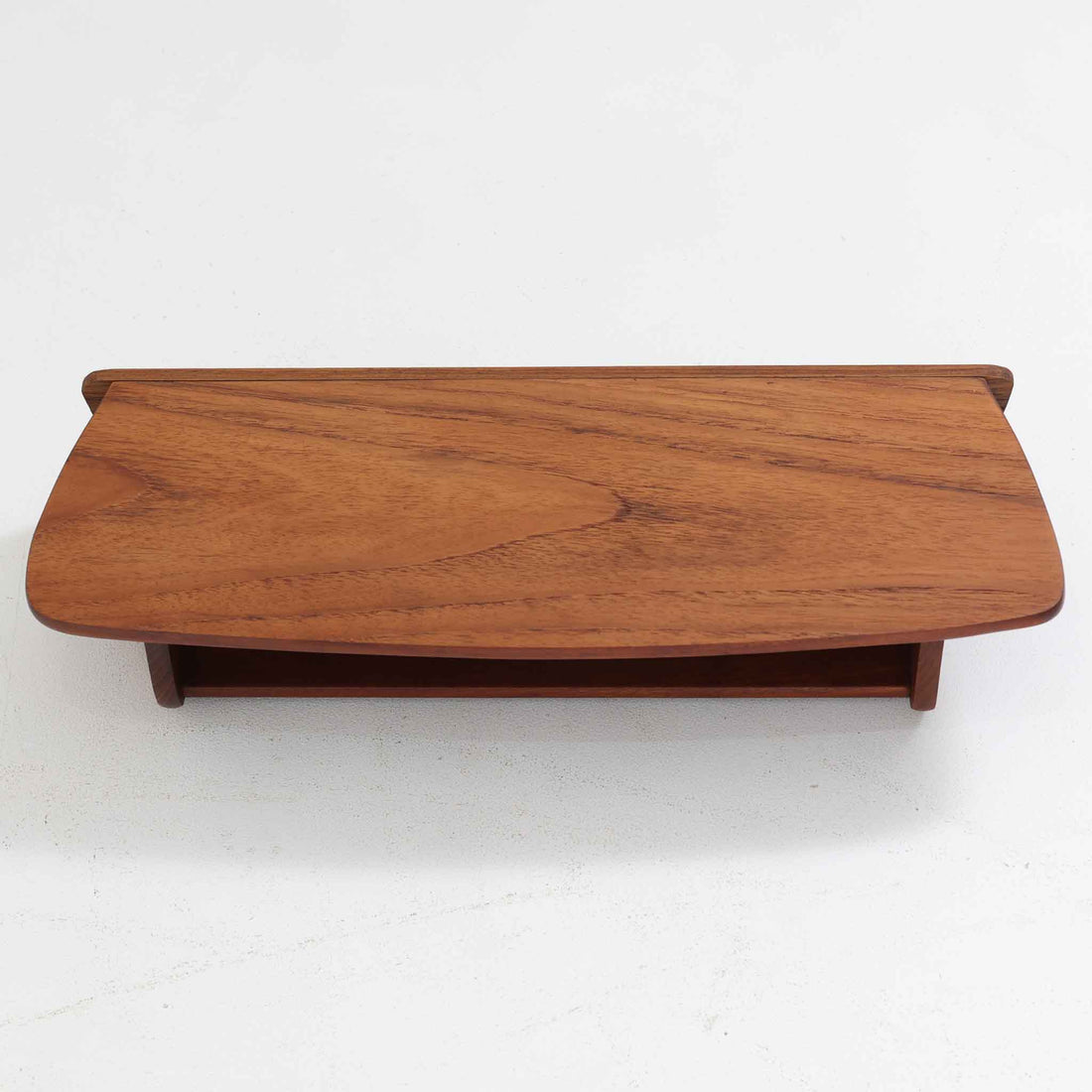 デンマーク製ウォールシェルフです。上質なチーク無垢材を使用し、滑らかなカーブを描く縁取りと丸みのあるフォルムが北欧家具らしい柔らかさを感じさせます。奥行きを抑えたコンパクトなサイズで、玄関や寝室、リビングのちょっとしたスペースにも取り付けやすい設計です。経年により深みを増したチーク材の美しい色合いが、壁面を上品に演出します。