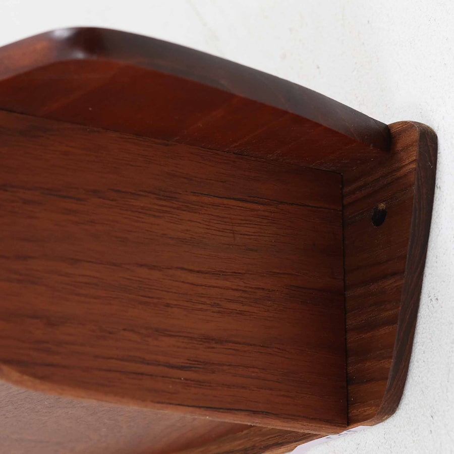 デンマーク製ウォールシェルフです。上質なチーク無垢材を使用し、滑らかなカーブを描く縁取りと丸みのあるフォルムが北欧家具らしい柔らかさを感じさせます。奥行きを抑えたコンパクトなサイズで、玄関や寝室、リビングのちょっとしたスペースにも取り付けやすい設計です。経年により深みを増したチーク材の美しい色合いが、壁面を上品に演出します。