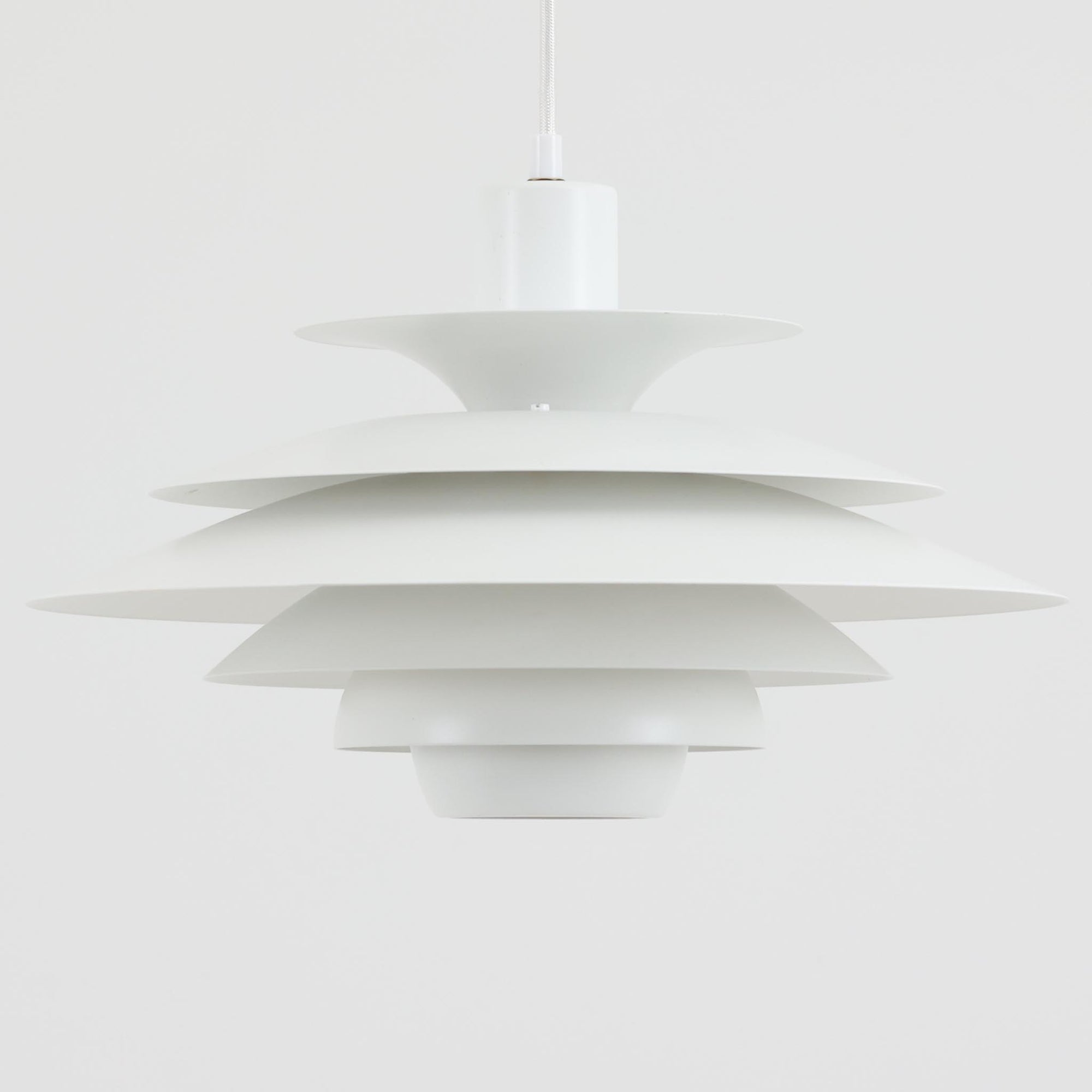 Jeka Metaltryk社製のペンダントライト「1039-H」です。直径41cmと存在感のあるサイズで、スチールを用いた重なり合うシェードが特徴的なデザイン。点灯時には多層のシェードを通して光が柔らかく拡散し、眩しさを抑えつつも温かみのある明かりを広げます。ホワイトカラーのシンプルかつモダンなフォルムは、ダイニングやリビングの主照明として空間に洗練された印象を与えます。北欧ビンテージらしい機能美と存在感を兼ね備えた逸品です。