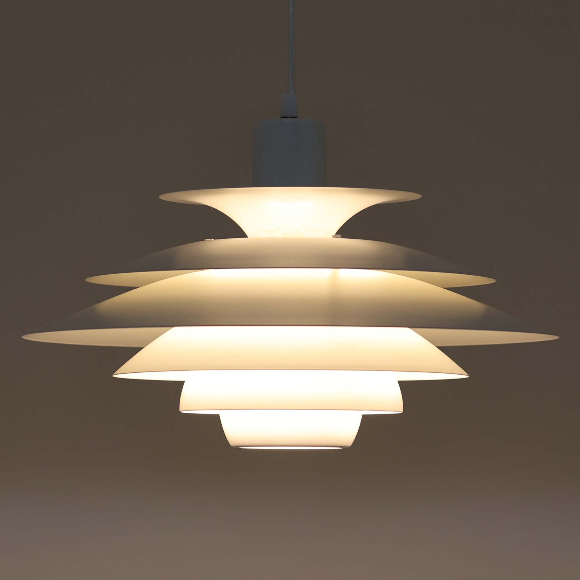 Jeka Metaltryk社製のペンダントライト「1039-H」です。直径41cmと存在感のあるサイズで、スチールを用いた重なり合うシェードが特徴的なデザイン。点灯時には多層のシェードを通して光が柔らかく拡散し、眩しさを抑えつつも温かみのある明かりを広げます。ホワイトカラーのシンプルかつモダンなフォルムは、ダイニングやリビングの主照明として空間に洗練された印象を与えます。北欧ビンテージらしい機能美と存在感を兼ね備えた逸品です。