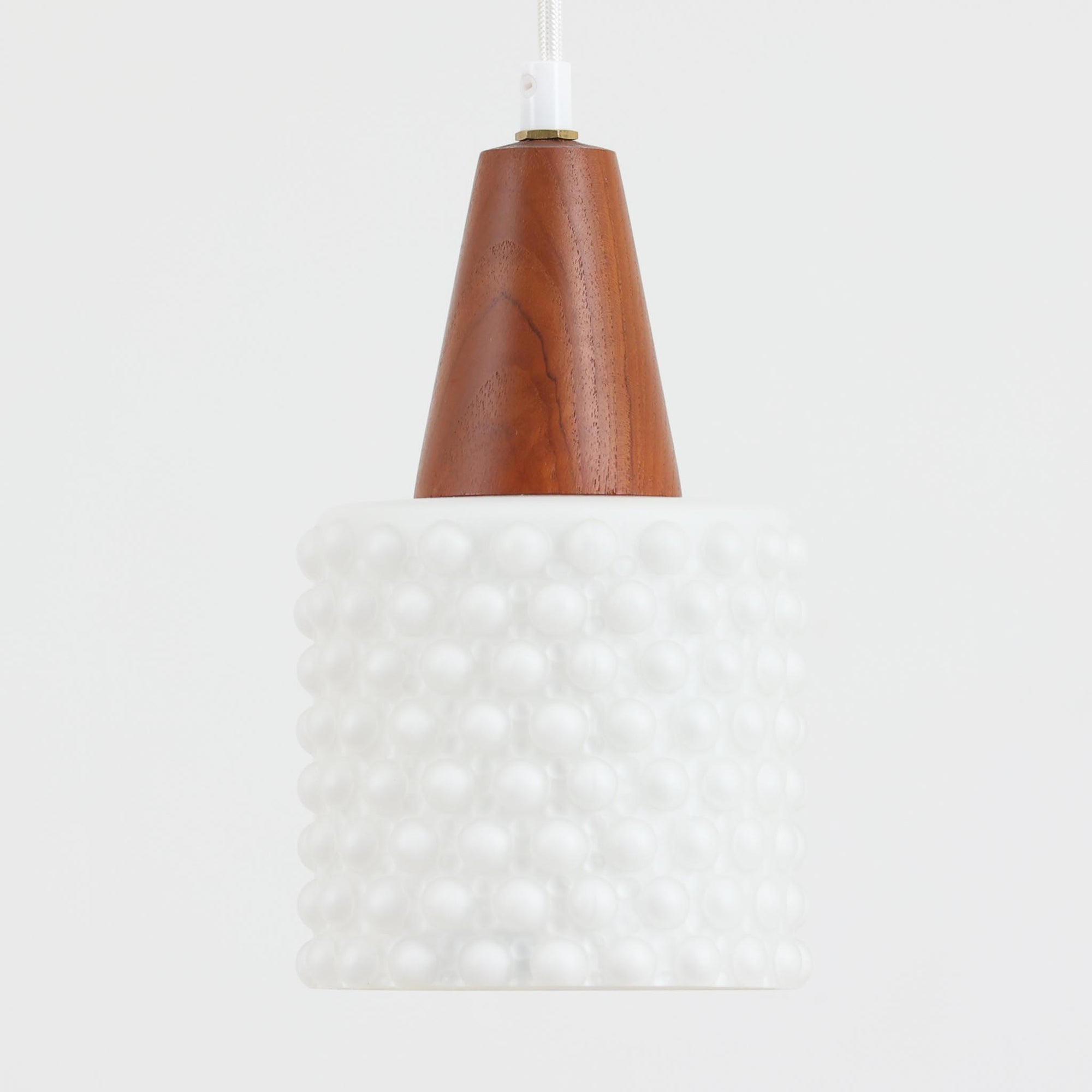 デンマーク製のペンダントライト、直径13cmです。ガラスシェードには立体的なドット模様が施され、点灯すると陰影が浮かび上がり独特の表情を生み出します。上部にはチーク材が用いられ、ガラスの繊細さと木の温もりが調和した北欧らしい意匠が魅力です。小ぶりなサイズながらも存在感があり、キッチンや廊下、ベッドサイドなど複数使いにも適しています。経年による素材の風合いがビンテージ品ならではの味わいを感じさせ、日常空間に個性を添える一品です。