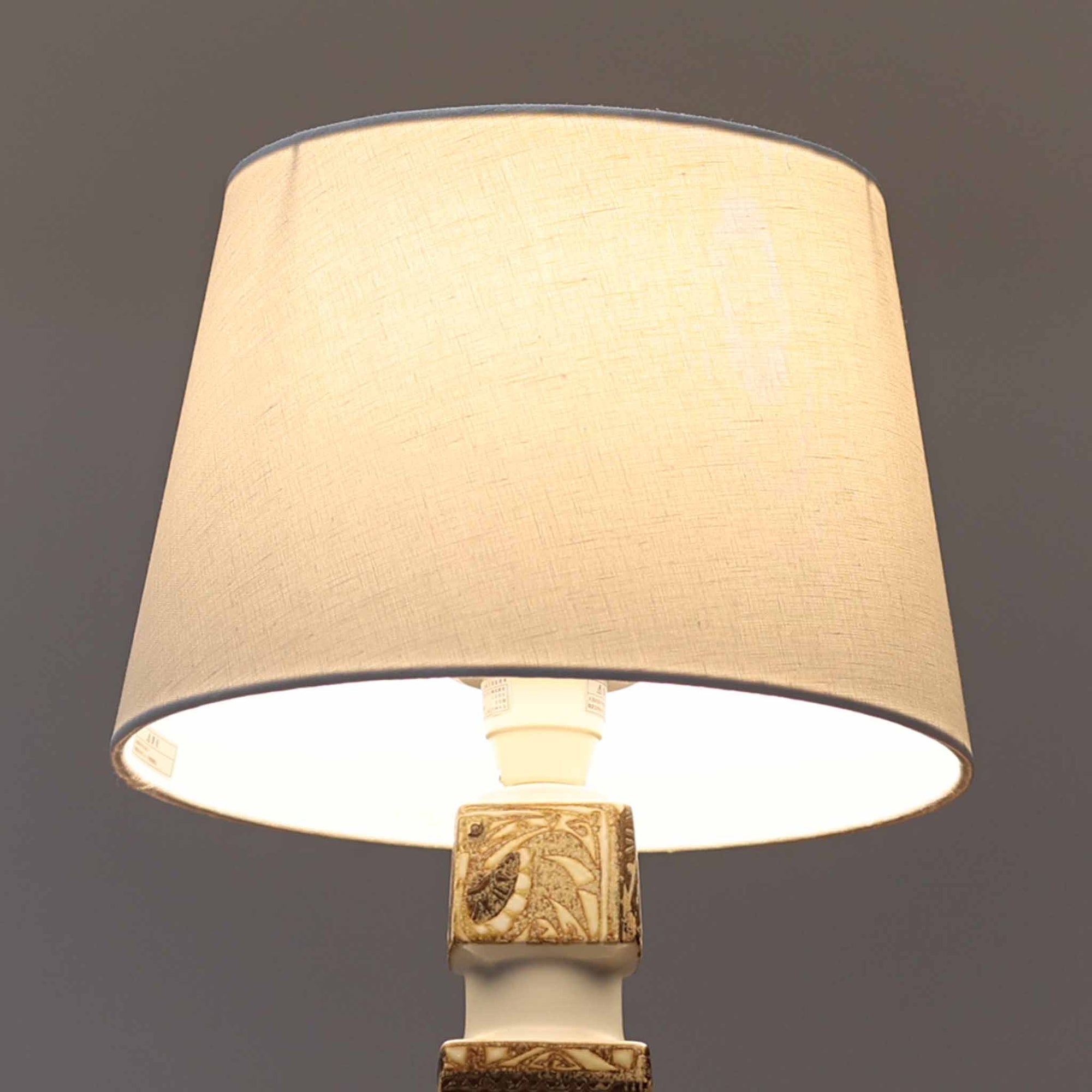 Nils Thorssonがデザインし、Royal Copenhagen社から発表された「BACA」シリーズのテーブルランプは、高さ39cmのバランスの取れたサイズ感で、北欧ビンテージらしい存在感を放ちます。陶磁器製のベースには細やかな装飾模様が施され、グラフィカルでありながら落ち着いた色調が空間に洗練された雰囲気を添えます。リネンシェードを透過する柔らかな光が温もりを演出し、リビングやベッドサイドに最適です。年月を経て深みを増した質感と工芸的な美しさを楽しめる一点物です。