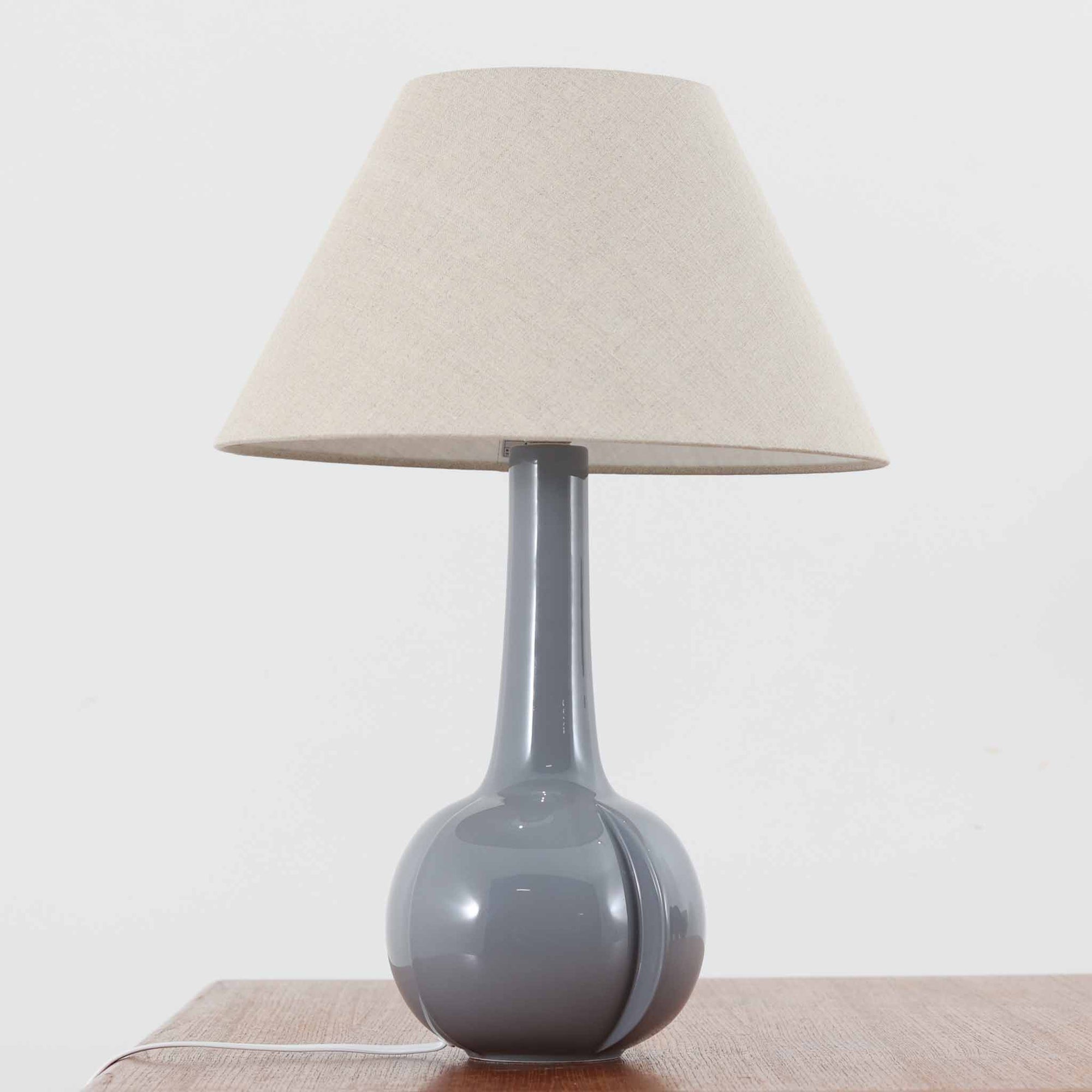 Royal Copenhagen社製のテーブルランプ「1013-3807」です。高さ50cmと存在感のある大きめサイズで、陶磁器ならではの艶やかな質感のベースにリネンシェードが組み合わされ、落ち着いた雰囲気を醸し出しています。クラシカルなフォルムに北欧らしい洗練されたデザインが融合し、点灯時には柔らかく温かな光が空間を包み込みます。リビングやベッドサイドのアクセントとしてはもちろん、インテリアオブジェとしても映える北欧ビンテージの逸品です。