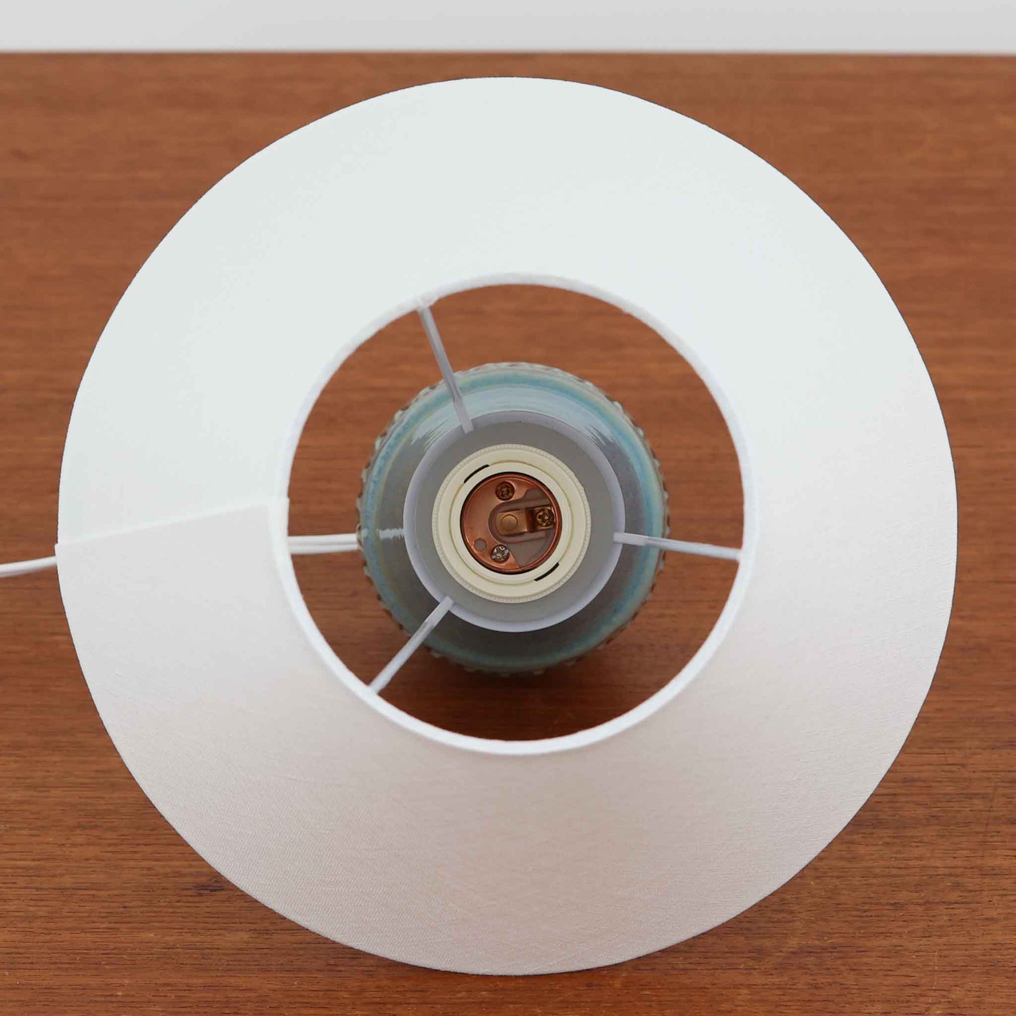 デンマークの名窯Michael Andersen &amp; Sonによる高さ29cmのテーブルランプは、北欧ビンテージらしい温もりと存在感を兼ね備えています。陶磁器製のベースにはブルーからブラウンへと移ろう釉薬が美しいグラデーションを描き、下部に施された幾何学的なレリーフ模様がデザインのアクセントとなっています。リネンシェードを透過する柔らかな光は、ベッドサイドやリビングに穏やかな雰囲気を添え、使うほどに味わいを深める一点物の魅力を楽しめます。