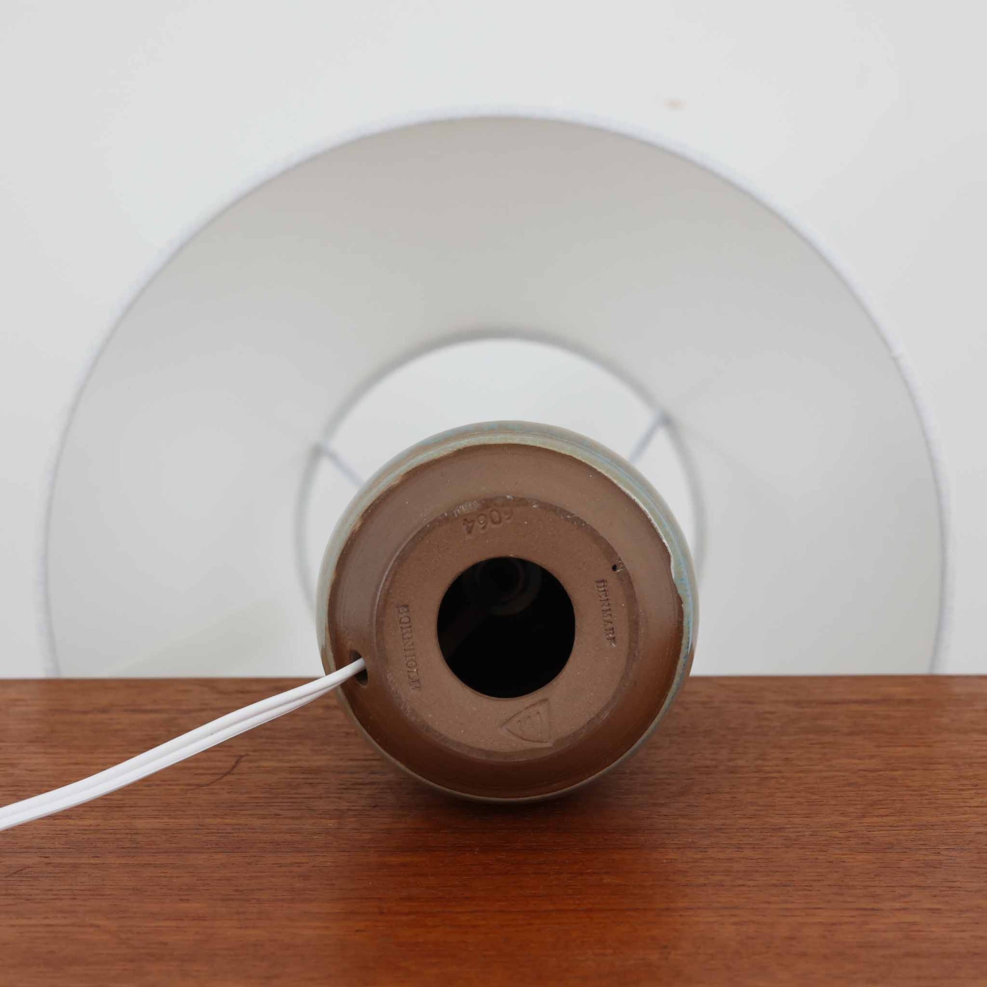 デンマークの名窯Michael Andersen &amp; Sonによる高さ29cmのテーブルランプは、北欧ビンテージらしい温もりと存在感を兼ね備えています。陶磁器製のベースにはブルーからブラウンへと移ろう釉薬が美しいグラデーションを描き、下部に施された幾何学的なレリーフ模様がデザインのアクセントとなっています。リネンシェードを透過する柔らかな光は、ベッドサイドやリビングに穏やかな雰囲気を添え、使うほどに味わいを深める一点物の魅力を楽しめます。