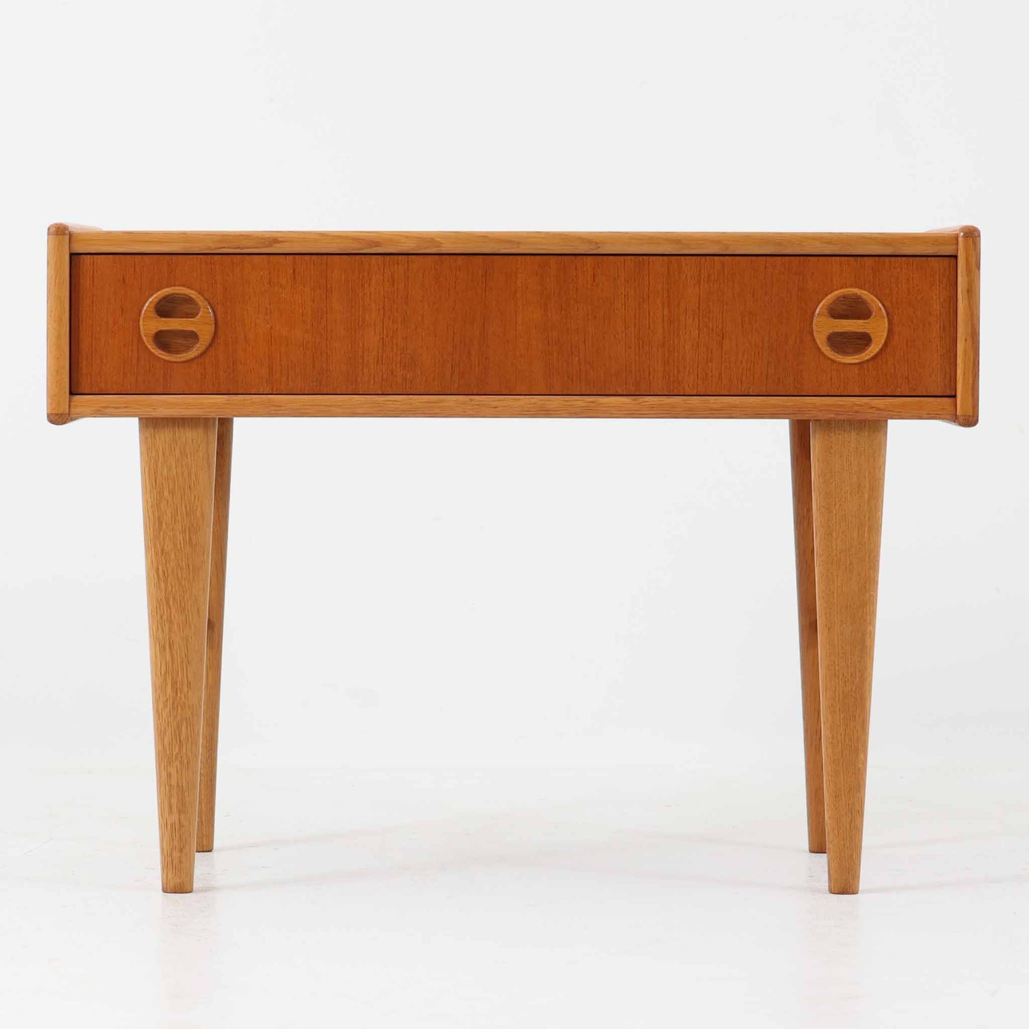 チーク材とオーク材を組み合わせたこちらの2段チェストは、幅70cmのコンパクトなサイズながら、北欧ビンテージ家具らしい洗練されたデザインが魅力です。丸型の埋め込み取手が愛らしいアクセントとなり、テーパー脚との調和が軽快な印象を与えます。引き出しは小物収納に適しており、ベッドサイドやリビングのサイドテーブルとしても活躍。素材のコントラストと経年による木肌の深みが、空間に温もりと個性を添える一品です。