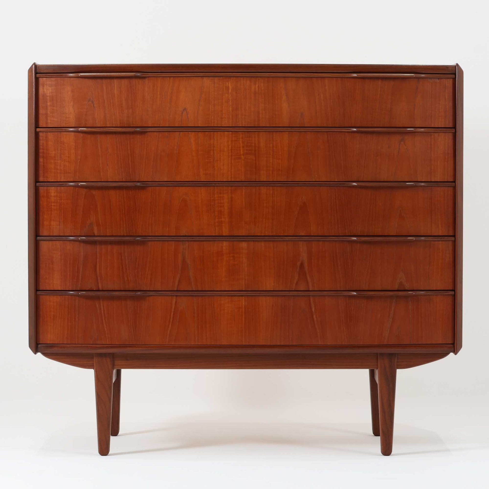 北欧ビンテージらしい端正な佇まいが魅力の5段チェストです。良質な木材を用いた本体は、横に流れる美しい木目に加え、角だけでなく前板を含む本体全体が緩やかな曲線を描く、有機的で上質なフォルムが特徴です。引き出し前板には手掛け一体型の彫り込みが施され、丸みを帯びた造形と相まって柔らかな印象を与えます。高い工作精度が感じられるクオリティの高い一台で、収納力に優れたサイズながら脚付き構造により軽やかさも備え、寝室やリビングの主収納として活躍します。Vordingborg Mobelfabrik社製と伝えられていますが確証はなく、メーカー不詳のビンテージ品としてご紹介します。経年変化によって深みを増した木肌が、空間に上質な存在感をもたらします。