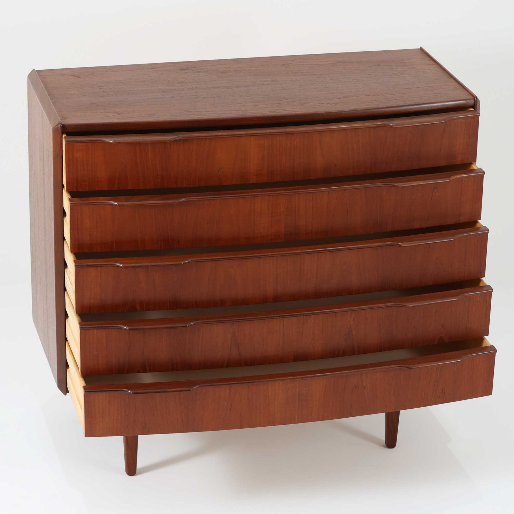 北欧ビンテージらしい端正な佇まいが魅力の5段チェストです。良質な木材を用いた本体は、横に流れる美しい木目に加え、角だけでなく前板を含む本体全体が緩やかな曲線を描く、有機的で上質なフォルムが特徴です。引き出し前板には手掛け一体型の彫り込みが施され、丸みを帯びた造形と相まって柔らかな印象を与えます。高い工作精度が感じられるクオリティの高い一台で、収納力に優れたサイズながら脚付き構造により軽やかさも備え、寝室やリビングの主収納として活躍します。Vordingborg Mobelfabrik社製と伝えられていますが確証はなく、メーカー不詳のビンテージ品としてご紹介します。経年変化によって深みを増した木肌が、空間に上質な存在感をもたらします。