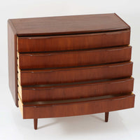 北欧ビンテージらしい端正な佇まいが魅力の5段チェストです。良質な木材を用いた本体は、横に流れる美しい木目に加え、角だけでなく前板を含む本体全体が緩やかな曲線を描く、有機的で上質なフォルムが特徴です。引き出し前板には手掛け一体型の彫り込みが施され、丸みを帯びた造形と相まって柔らかな印象を与えます。高い工作精度が感じられるクオリティの高い一台で、収納力に優れたサイズながら脚付き構造により軽やかさも備え、寝室やリビングの主収納として活躍します。Vordingborg Mobelfabrik社製と伝えられていますが確証はなく、メーカー不詳のビンテージ品としてご紹介します。経年変化によって深みを増した木肌が、空間に上質な存在感をもたらします。