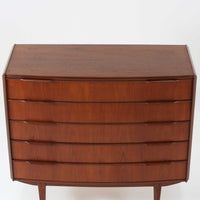 北欧ビンテージらしい端正な佇まいが魅力の5段チェストです。良質な木材を用いた本体は、横に流れる美しい木目に加え、角だけでなく前板を含む本体全体が緩やかな曲線を描く、有機的で上質なフォルムが特徴です。引き出し前板には手掛け一体型の彫り込みが施され、丸みを帯びた造形と相まって柔らかな印象を与えます。高い工作精度が感じられるクオリティの高い一台で、収納力に優れたサイズながら脚付き構造により軽やかさも備え、寝室やリビングの主収納として活躍します。Vordingborg Mobelfabrik社製と伝えられていますが確証はなく、メーカー不詳のビンテージ品としてご紹介します。経年変化によって深みを増した木肌が、空間に上質な存在感をもたらします。