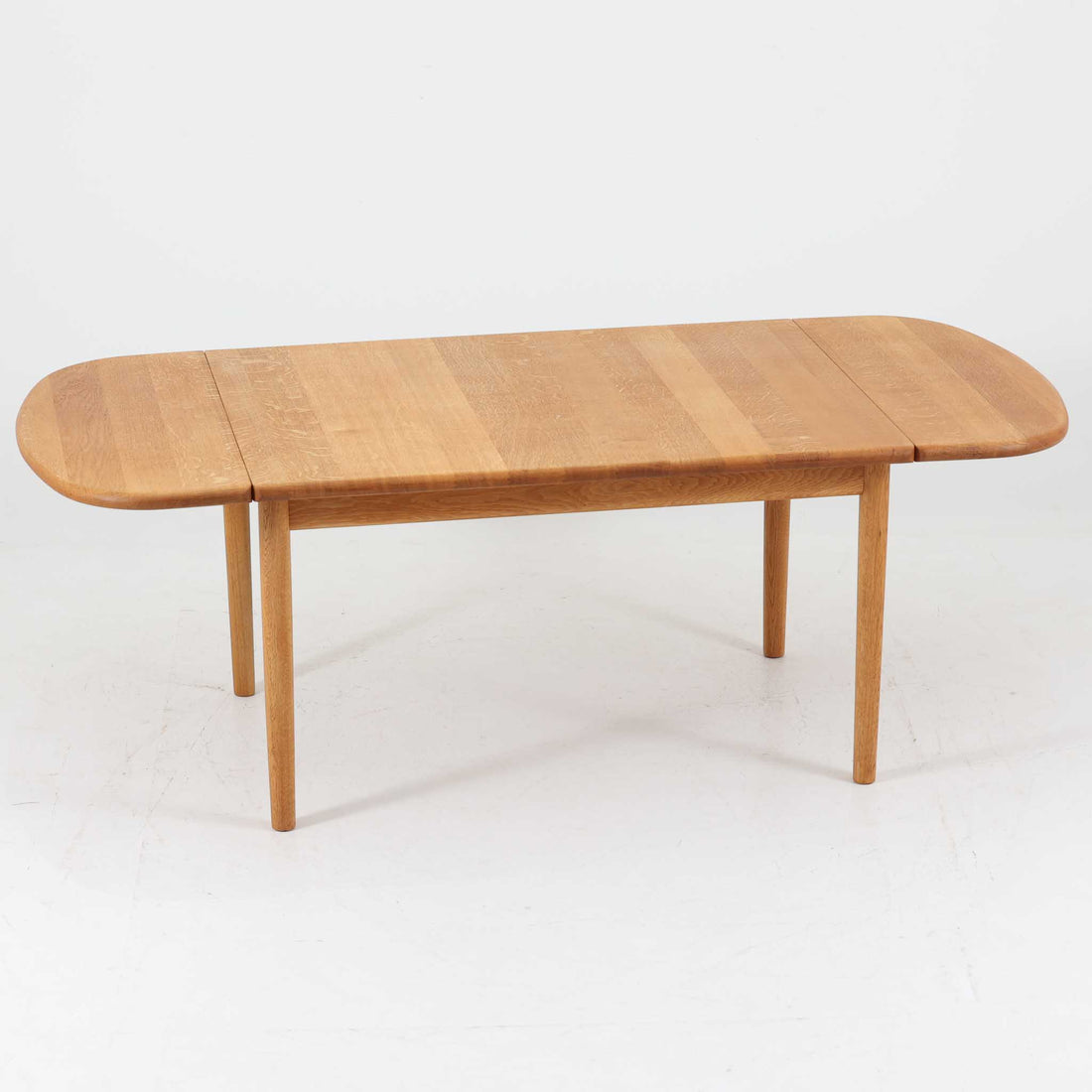 Hans J. Wegnerがデザインし、Getama社より製造されたセンターテーブル「GE82」は、丸脚の意匠が特徴で、四角脚の「GE85」と同時期にデザインされたといわれています。バタフライ構造による拡張機能を備えた北欧ビンテージ家具で、オーク無垢材を贅沢に使用し、幅103cmから160cmへと用途に応じてサイズ調整が可能。普段はコンパクトに、来客時には広々と使える実用性が魅力です。シンプルで力強いフォルムと無垢材ならではの豊かな木目は、年月を経て一層の味わいを増し、空間に温もりと存在感を添えます。