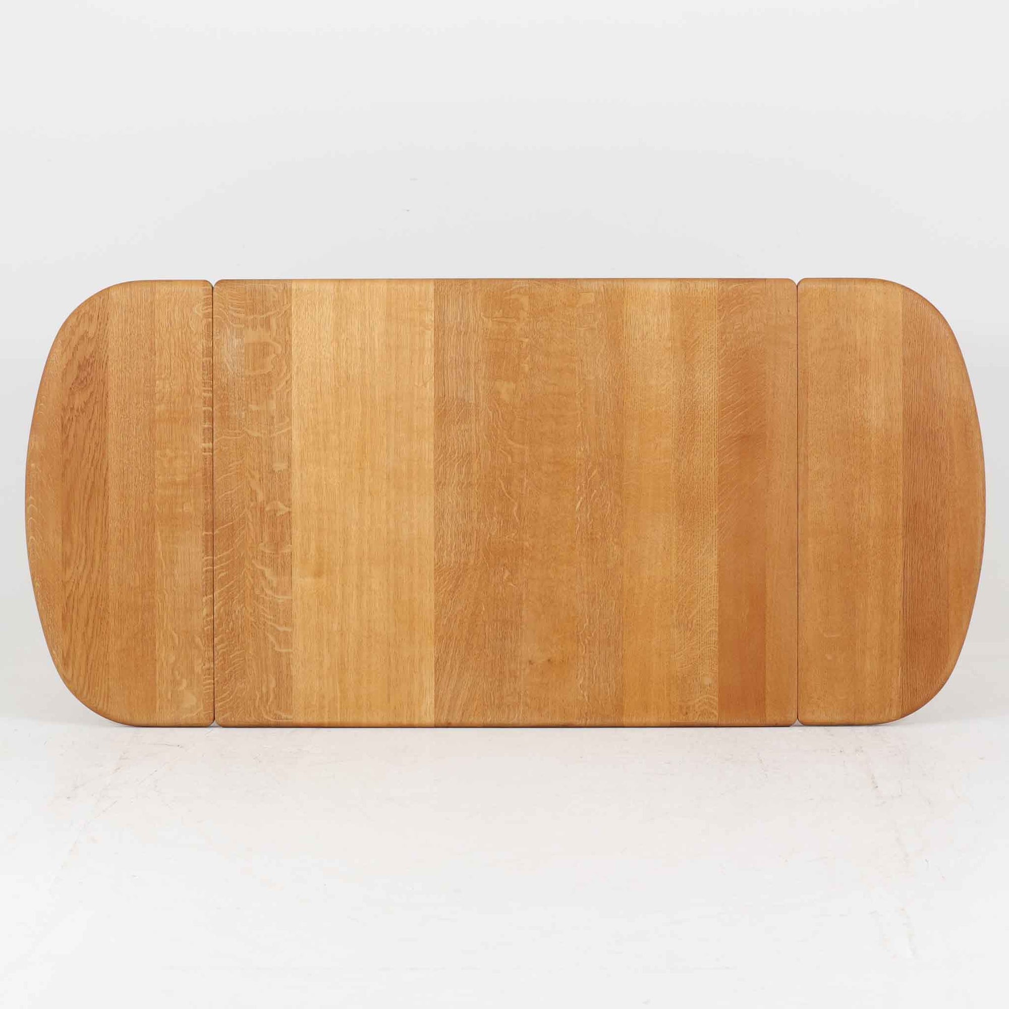 Hans J. Wegnerがデザインし、Getama社より製造されたセンターテーブル「GE82」は、丸脚の意匠が特徴で、四角脚の「GE85」と同時期にデザインされたといわれています。バタフライ構造による拡張機能を備えた北欧ビンテージ家具で、オーク無垢材を贅沢に使用し、幅103cmから160cmへと用途に応じてサイズ調整が可能。普段はコンパクトに、来客時には広々と使える実用性が魅力です。シンプルで力強いフォルムと無垢材ならではの豊かな木目は、年月を経て一層の味わいを増し、空間に温もりと存在感を添えます。