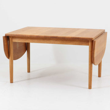 Hans J. Wegnerがデザインし、Getama社より製造されたセンターテーブル「GE82」は、丸脚の意匠が特徴で、四角脚の「GE85」と同時期にデザインされたといわれています。バタフライ構造による拡張機能を備えた北欧ビンテージ家具で、オーク無垢材を贅沢に使用し、幅103cmから160cmへと用途に応じてサイズ調整が可能。普段はコンパクトに、来客時には広々と使える実用性が魅力です。シンプルで力強いフォルムと無垢材ならではの豊かな木目は、年月を経て一層の味わいを増し、空間に温もりと存在感を添えます。