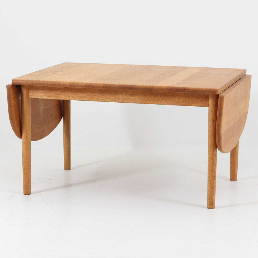 Hans J. Wegnerがデザインし、Getama社より製造されたセンターテーブル「GE82」は、丸脚の意匠が特徴で、四角脚の「GE85」と同時期にデザインされたといわれています。バタフライ構造による拡張機能を備えた北欧ビンテージ家具で、オーク無垢材を贅沢に使用し、幅103cmから160cmへと用途に応じてサイズ調整が可能。普段はコンパクトに、来客時には広々と使える実用性が魅力です。シンプルで力強いフォルムと無垢材ならではの豊かな木目は、年月を経て一層の味わいを増し、空間に温もりと存在感を添えます。