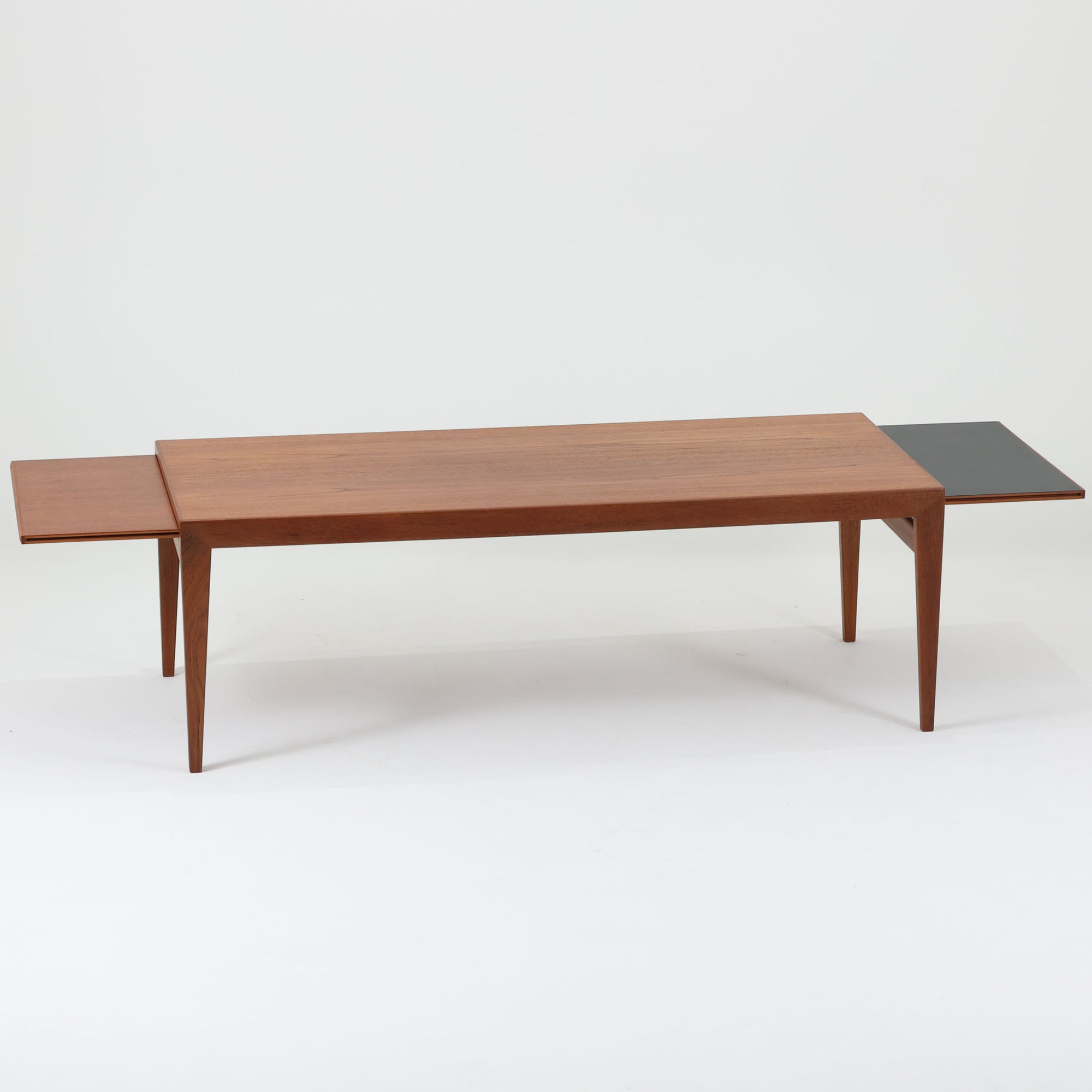 チーク材を用いたデンマーク製の拡張板付きセンターテーブルです。直線的で軽やかなフレーム構造と、脚部から天板へとつながる端正な接合部に北欧ビンテージらしい丁寧なつくりが感じられます。拡張板を引き出すことで天板幅を大きく広げることができ、来客時や作業スペースとしても柔軟に対応します。深みを増したチークの色合いと美しい木目が空間に落ち着きを与え、リビングの主役として長く愛用できる一台です。拡張板はチーク材のほか、黒のラミネート仕上げの2種類が備わっており、用途に応じて使い分けが可能です。ラミネート面は輪染みがつきにくく、作業用や来客時にも気兼ねなく使える実用性を備えています。