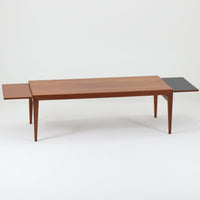 チーク材を用いたデンマーク製の拡張板付きセンターテーブルです。直線的で軽やかなフレーム構造と、脚部から天板へとつながる端正な接合部に北欧ビンテージらしい丁寧なつくりが感じられます。拡張板を引き出すことで天板幅を大きく広げることができ、来客時や作業スペースとしても柔軟に対応します。深みを増したチークの色合いと美しい木目が空間に落ち着きを与え、リビングの主役として長く愛用できる一台です。拡張板はチーク材のほか、黒のラミネート仕上げの2種類が備わっており、用途に応じて使い分けが可能です。ラミネート面は輪染みがつきにくく、作業用や来客時にも気兼ねなく使える実用性を備えています。