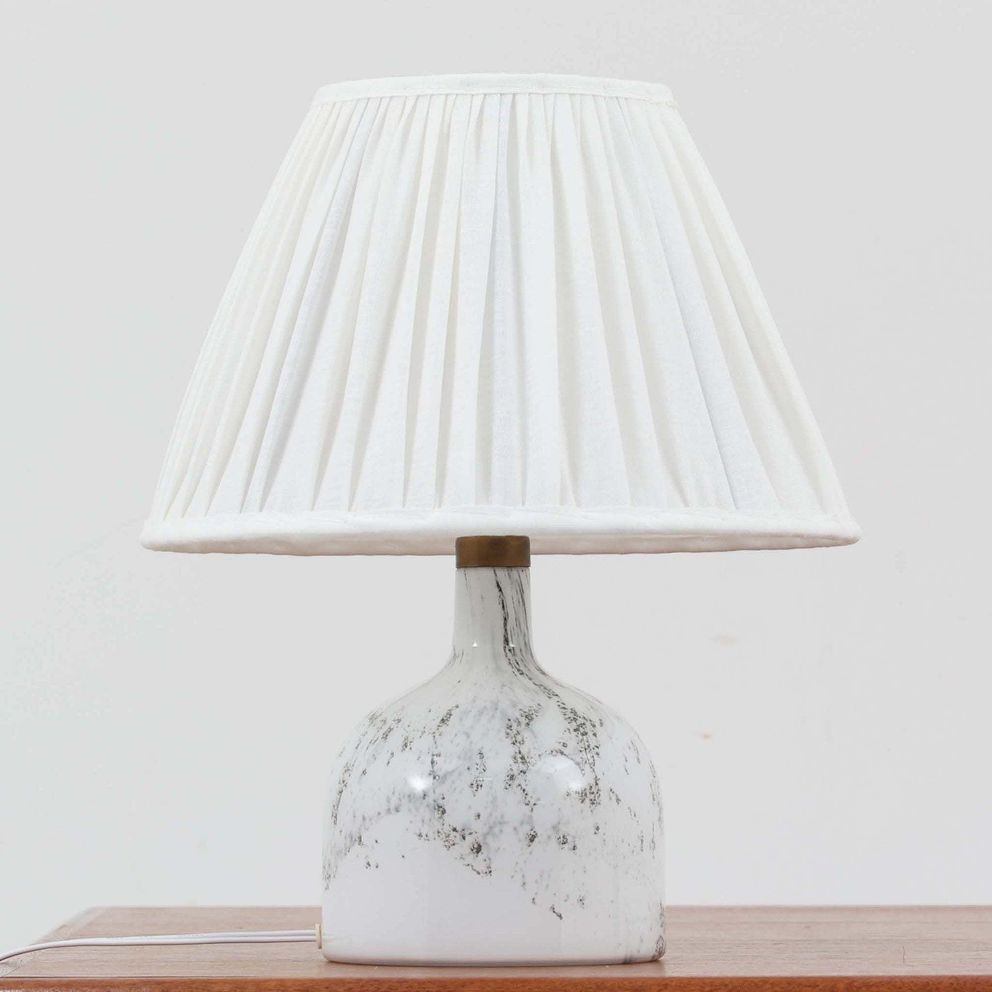 デンマークを代表するガラスメーカー、Holmegaard社よりMichael Bangが手掛けた「LAMP ART」テーブルランプは、高さ40cmのバランス良いサイズ感で、北欧ビンテージの魅力を放ちます。ベースはホワイトガラスにマーブル状の模様が施され、柔らかな光を映し出す造形美が特徴です。真鍮のパーツがアクセントとなり、リネンシェードを透過する光は空間に穏やかな温もりを添えます。洗練されたデザインと職人技が調和した一点物で、リビングや寝室の雰囲気を格上げする逸品です。