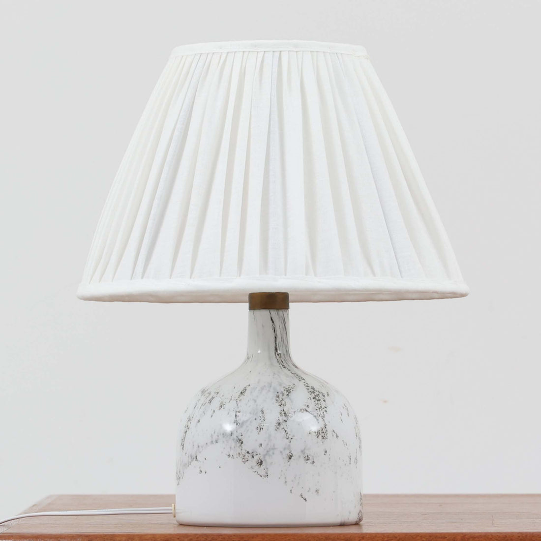 デンマークを代表するガラスメーカー、Holmegaard社よりMichael Bangが手掛けた「LAMP ART」テーブルランプは、高さ40cmのバランス良いサイズ感で、北欧ビンテージの魅力を放ちます。ベースはホワイトガラスにマーブル状の模様が施され、柔らかな光を映し出す造形美が特徴です。真鍮のパーツがアクセントとなり、リネンシェードを透過する光は空間に穏やかな温もりを添えます。洗練されたデザインと職人技が調和した一点物で、リビングや寝室の雰囲気を格上げする逸品です。