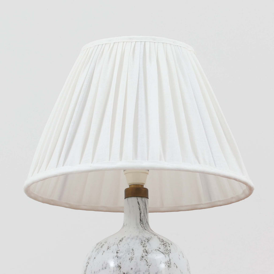 デンマークを代表するガラスメーカー、Holmegaard社よりMichael Bangが手掛けた「LAMP ART」テーブルランプは、高さ40cmのバランス良いサイズ感で、北欧ビンテージの魅力を放ちます。ベースはホワイトガラスにマーブル状の模様が施され、柔らかな光を映し出す造形美が特徴です。真鍮のパーツがアクセントとなり、リネンシェードを透過する光は空間に穏やかな温もりを添えます。洗練されたデザインと職人技が調和した一点物で、リビングや寝室の雰囲気を格上げする逸品です。
