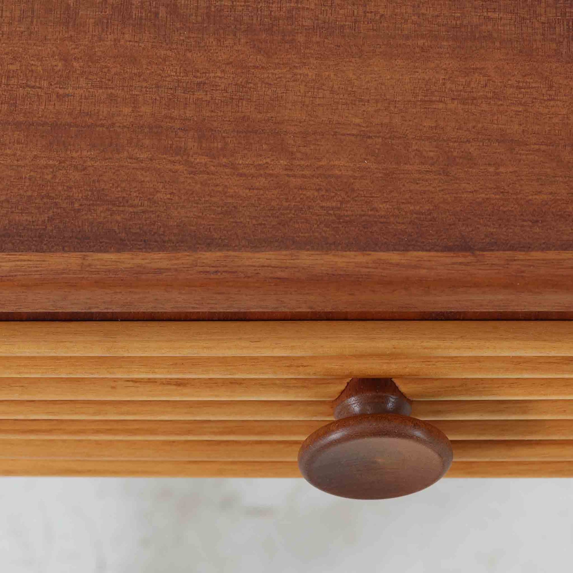 デンマークのサイドチェストです。アフロモシア材の落ち着いた色味の本体に、ビーチ材で成形された横溝装飾の引き出し前板がアクセントとなり、シンプルな構造の中にリズム感のある表情を生み出しています。幅54cmのコンパクトなサイズで、ベッドサイドやソファ脇、玄関先などにも取り入れやすく、引き出し付きで実用性も十分です。経年により深まった木肌の風合いと丁寧なつくりが、北欧ビンテージらしい静かな存在感を空間に添えてくれます。