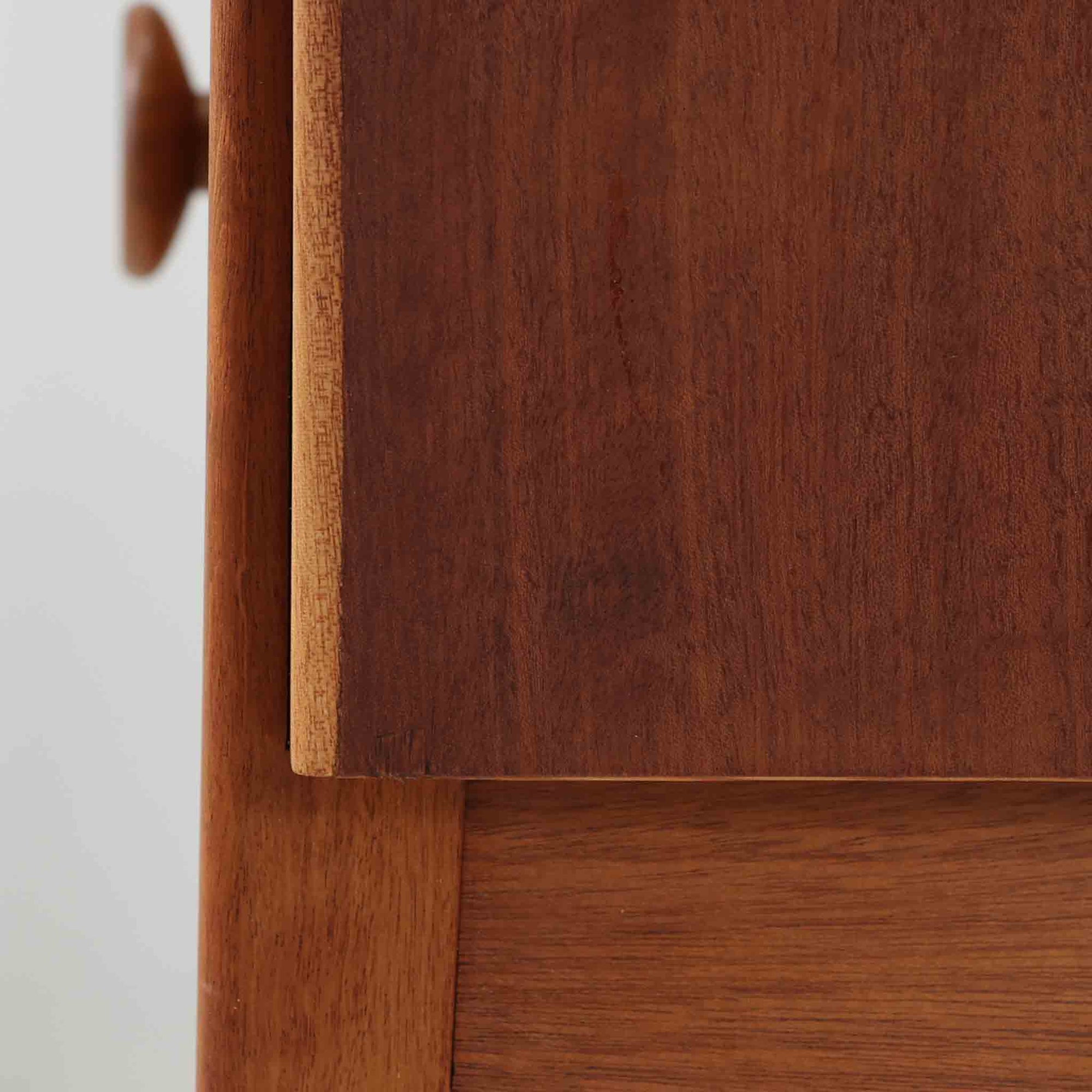 デンマークのサイドチェストです。アフロモシア材の落ち着いた色味の本体に、ビーチ材で成形された横溝装飾の引き出し前板がアクセントとなり、シンプルな構造の中にリズム感のある表情を生み出しています。幅54cmのコンパクトなサイズで、ベッドサイドやソファ脇、玄関先などにも取り入れやすく、引き出し付きで実用性も十分です。経年により深まった木肌の風合いと丁寧なつくりが、北欧ビンテージらしい静かな存在感を空間に添えてくれます。