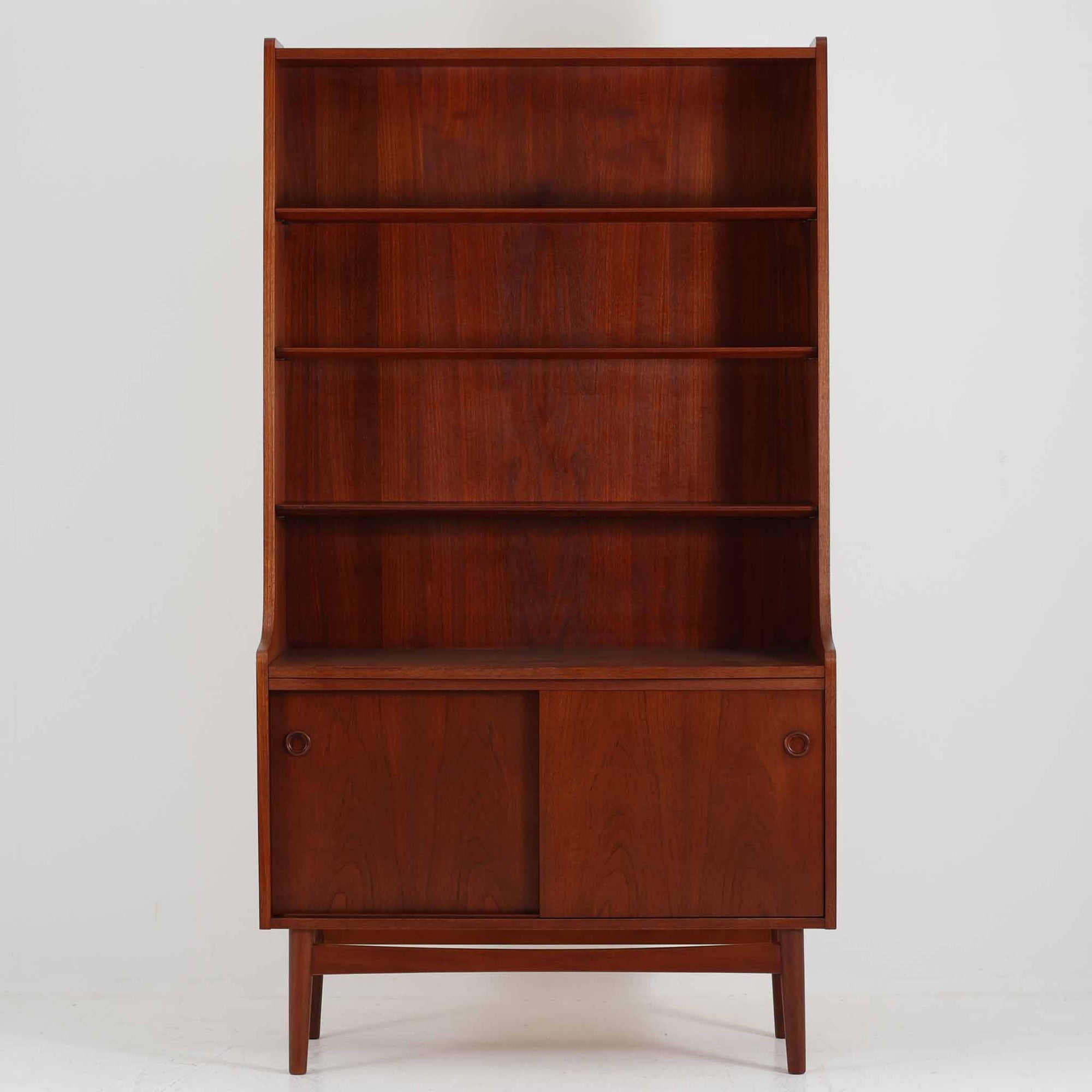 Johannes Sorth（ヨハネス・ソース）によるデザインで、Nexo Mobelfabrik社より製造されたチーク材のディスプレイシェルフです。上部の棚は本やオブジェを美しく飾ることができ、下部には引き戸収納を備え、実用性にも優れています。緩やかな曲線を描く側面のデザインが柔らかな印象を与え、北欧家具らしい温もりと機能美が感じられる一台です。脚部の細身のフォルムが軽やかさを演出し、リビングや書斎、ダイニングなど幅広い空間に調和します。