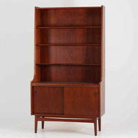 Johannes Sorth（ヨハネス・ソース）によるデザインで、Nexo Mobelfabrik社より製造されたチーク材のディスプレイシェルフです。上部の棚は本やオブジェを美しく飾ることができ、下部には引き戸収納を備え、実用性にも優れています。緩やかな曲線を描く側面のデザインが柔らかな印象を与え、北欧家具らしい温もりと機能美が感じられる一台です。脚部の細身のフォルムが軽やかさを演出し、リビングや書斎、ダイニングなど幅広い空間に調和します。