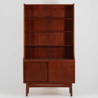 Johannes Sorth（ヨハネス・ソース）によるデザインで、Nexo Mobelfabrik社より製造されたチーク材のディスプレイシェルフです。上部の棚は本やオブジェを美しく飾ることができ、下部には引き戸収納を備え、実用性にも優れています。緩やかな曲線を描く側面のデザインが柔らかな印象を与え、北欧家具らしい温もりと機能美が感じられる一台です。脚部の細身のフォルムが軽やかさを演出し、リビングや書斎、ダイニングなど幅広い空間に調和します。