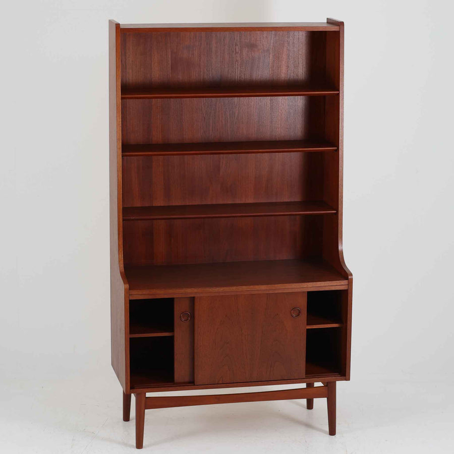 Johannes Sorth（ヨハネス・ソース）によるデザインで、Nexo Mobelfabrik社より製造されたチーク材のディスプレイシェルフです。上部の棚は本やオブジェを美しく飾ることができ、下部には引き戸収納を備え、実用性にも優れています。緩やかな曲線を描く側面のデザインが柔らかな印象を与え、北欧家具らしい温もりと機能美が感じられる一台です。脚部の細身のフォルムが軽やかさを演出し、リビングや書斎、ダイニングなど幅広い空間に調和します。