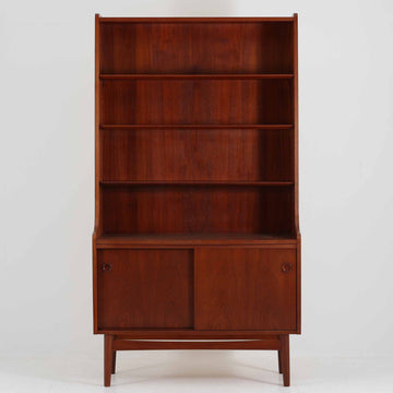 Johannes Sorth（ヨハネス・ソース）によるデザインで、Nexo Mobelfabrik社より製造されたチーク材のディスプレイシェルフです。上部の棚は本やオブジェを美しく飾ることができ、下部には引き戸収納を備え、実用性にも優れています。緩やかな曲線を描く側面のデザインが柔らかな印象を与え、北欧家具らしい温もりと機能美が感じられる一台です。脚部の細身のフォルムが軽やかさを演出し、リビングや書斎、ダイニングなど幅広い空間に調和します。