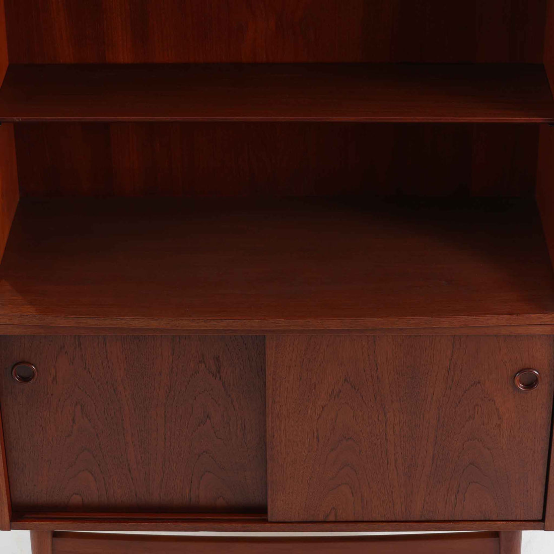 Johannes Sorth（ヨハネス・ソース）によるデザインで、Nexo Mobelfabrik社より製造されたチーク材のディスプレイシェルフです。上部の棚は本やオブジェを美しく飾ることができ、下部には引き戸収納を備え、実用性にも優れています。緩やかな曲線を描く側面のデザインが柔らかな印象を与え、北欧家具らしい温もりと機能美が感じられる一台です。脚部の細身のフォルムが軽やかさを演出し、リビングや書斎、ダイニングなど幅広い空間に調和します。