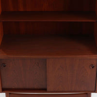 Johannes Sorth（ヨハネス・ソース）によるデザインで、Nexo Mobelfabrik社より製造されたチーク材のディスプレイシェルフです。上部の棚は本やオブジェを美しく飾ることができ、下部には引き戸収納を備え、実用性にも優れています。緩やかな曲線を描く側面のデザインが柔らかな印象を与え、北欧家具らしい温もりと機能美が感じられる一台です。脚部の細身のフォルムが軽やかさを演出し、リビングや書斎、ダイニングなど幅広い空間に調和します。