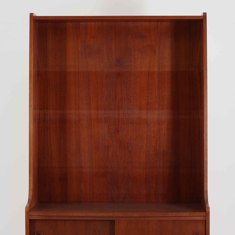 Johannes Sorth（ヨハネス・ソース）によるデザインで、Nexo Mobelfabrik社より製造されたチーク材のディスプレイシェルフです。上部の棚は本やオブジェを美しく飾ることができ、下部には引き戸収納を備え、実用性にも優れています。緩やかな曲線を描く側面のデザインが柔らかな印象を与え、北欧家具らしい温もりと機能美が感じられる一台です。脚部の細身のフォルムが軽やかさを演出し、リビングや書斎、ダイニングなど幅広い空間に調和します。