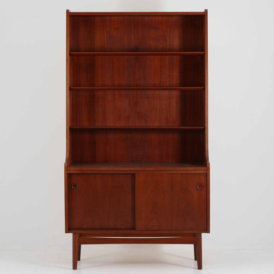 Johannes Sorth（ヨハネス・ソース）によるデザインで、Nexo Mobelfabrik社より製造されたチーク材のディスプレイシェルフです。上部の棚は本やオブジェを美しく飾ることができ、下部には引き戸収納を備え、実用性にも優れています。緩やかな曲線を描く側面のデザインが柔らかな印象を与え、北欧家具らしい温もりと機能美が感じられる一台です。脚部の細身のフォルムが軽やかさを演出し、リビングや書斎、ダイニングなど幅広い空間に調和します。