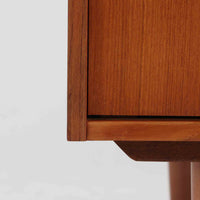 こちらの小ぶりなボードは、温かみのあるチーク材を用いたすっきりとした佇まいが魅力の北欧ビンテージ家具で、スライド扉を開くと左右に棚板付きの収納スペースが現れ、日用品や小物を効率よく整理できます。直線的な箱型の構造に、細身でテーパーの効いた脚部が軽やかな印象を添え、コンパクトながら存在感のある設計が空間に落ち着いたアクセントをもたらします。経年で深まった木肌の質感も味わい深く、リビングや玄関脇のサイド収納としても取り入れやすい一台です。