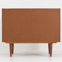 こちらの小ぶりなボードは、温かみのあるチーク材を用いたすっきりとした佇まいが魅力の北欧ビンテージ家具で、スライド扉を開くと左右に棚板付きの収納スペースが現れ、日用品や小物を効率よく整理できます。直線的な箱型の構造に、細身でテーパーの効いた脚部が軽やかな印象を添え、コンパクトながら存在感のある設計が空間に落ち着いたアクセントをもたらします。経年で深まった木肌の質感も味わい深く、リビングや玄関脇のサイド収納としても取り入れやすい一台です。