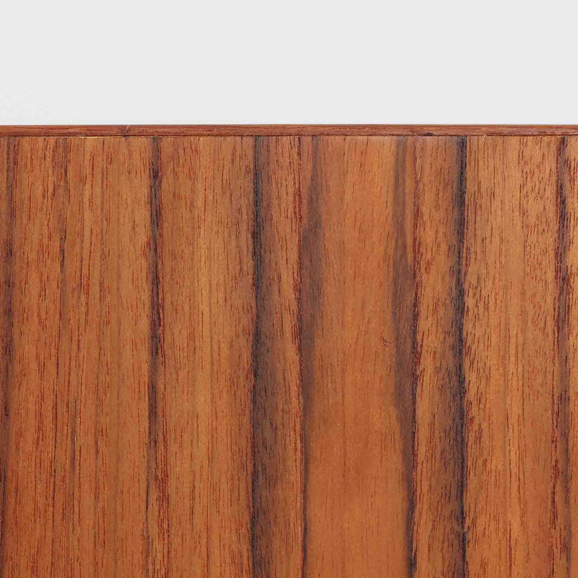 こちらの小ぶりなボードは、温かみのあるチーク材を用いたすっきりとした佇まいが魅力の北欧ビンテージ家具で、スライド扉を開くと左右に棚板付きの収納スペースが現れ、日用品や小物を効率よく整理できます。直線的な箱型の構造に、細身でテーパーの効いた脚部が軽やかな印象を添え、コンパクトながら存在感のある設計が空間に落ち着いたアクセントをもたらします。経年で深まった木肌の質感も味わい深く、リビングや玄関脇のサイド収納としても取り入れやすい一台です。