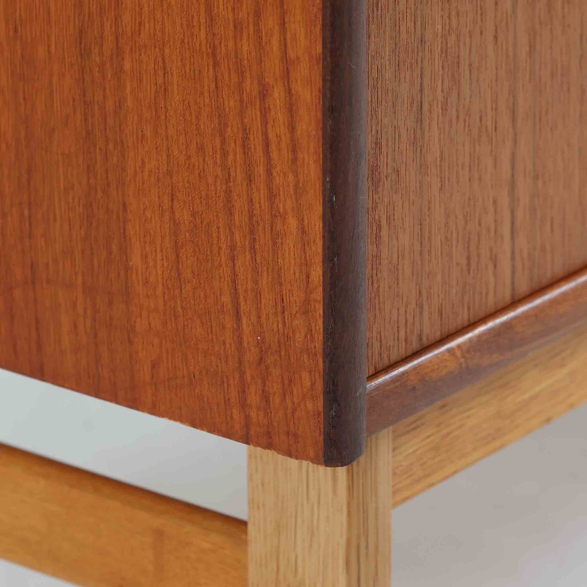 スウェーデン製のチーク材とオーク材を組み合わせたディスプレイシェルフです。幅90cmと程よいサイズ感で、上部の棚は書籍やオブジェの展示に適し、下部の引き戸収納は日用品や小物をすっきりと収めることができます。丸みを帯びた取っ手が温かみのあるアクセントとなり、北欧家具らしいシンプルで実用的なデザインを際立たせています。経年によって深みを増したチークの木目とオークのコントラストが上品な存在感を放ち、リビングや書斎の空間に落ち着いた雰囲気を添えるビンテージ家具です。