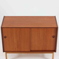 スウェーデン製のチーク材とオーク材を組み合わせたディスプレイシェルフです。幅90cmと程よいサイズ感で、上部の棚は書籍やオブジェの展示に適し、下部の引き戸収納は日用品や小物をすっきりと収めることができます。丸みを帯びた取っ手が温かみのあるアクセントとなり、北欧家具らしいシンプルで実用的なデザインを際立たせています。経年によって深みを増したチークの木目とオークのコントラストが上品な存在感を放ち、リビングや書斎の空間に落ち着いた雰囲気を添えるビンテージ家具です。