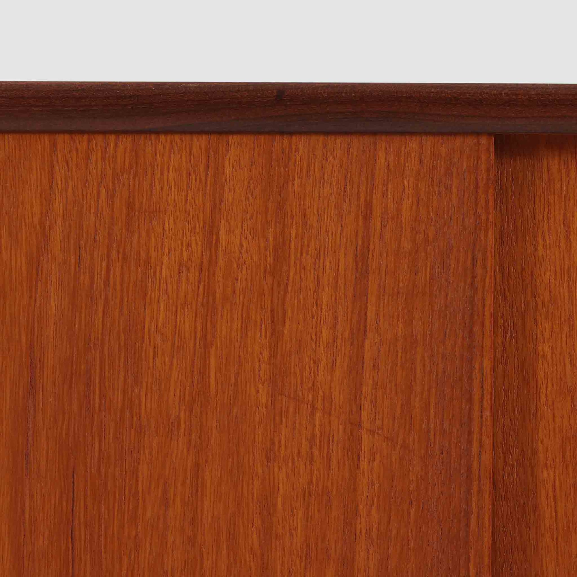 スウェーデン製のディスプレイシェルフです。上段には3段のオープンシェルフが設けられ、本や雑貨、オブジェなどを美しくディスプレイできます。下段にはスライド扉収納が備わり、内部の棚板によって整理しやすく、見せたくない収納にも便利です。チーク材の温もりある木目と、丸い掘り込み取っ手の柔らかなデザインが印象的で、北欧家具らしい穏やかな雰囲気を演出します。背面のグリーンの化粧板が空間に個性を添え、飾るアイテムをより際立たせます。本体にはチーク材、脚部にはオーク材が使用されており、素材のコントラストも魅力のひとつです。下段収納部の棚板にわずかな反りがありますが、裏返して使用することで目立たなくなります。軽やかな佇まいと実用性を兼ね備えた、北欧ビンテージらしい一台です。