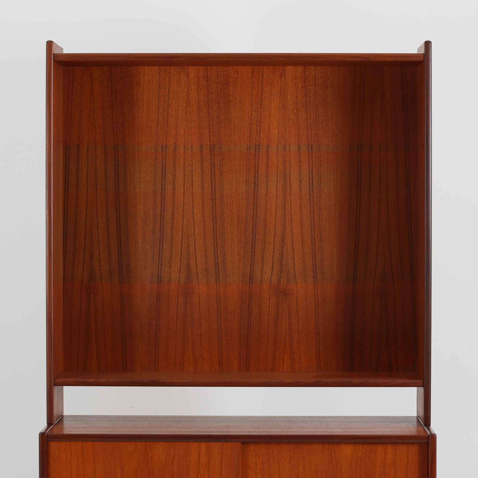 スウェーデン製のディスプレイシェルフです。上段には3段のオープンシェルフが設けられ、本や雑貨、オブジェなどを美しくディスプレイできます。下段にはスライド扉収納が備わり、内部の棚板によって整理しやすく、見せたくない収納にも便利です。チーク材の温もりある木目と、丸い掘り込み取っ手の柔らかなデザインが印象的で、北欧家具らしい穏やかな雰囲気を演出します。背面のグリーンの化粧板が空間に個性を添え、飾るアイテムをより際立たせます。本体にはチーク材、脚部にはオーク材が使用されており、素材のコントラストも魅力のひとつです。下段収納部の棚板にわずかな反りがありますが、裏返して使用することで目立たなくなります。軽やかな佇まいと実用性を兼ね備えた、北欧ビンテージらしい一台です。