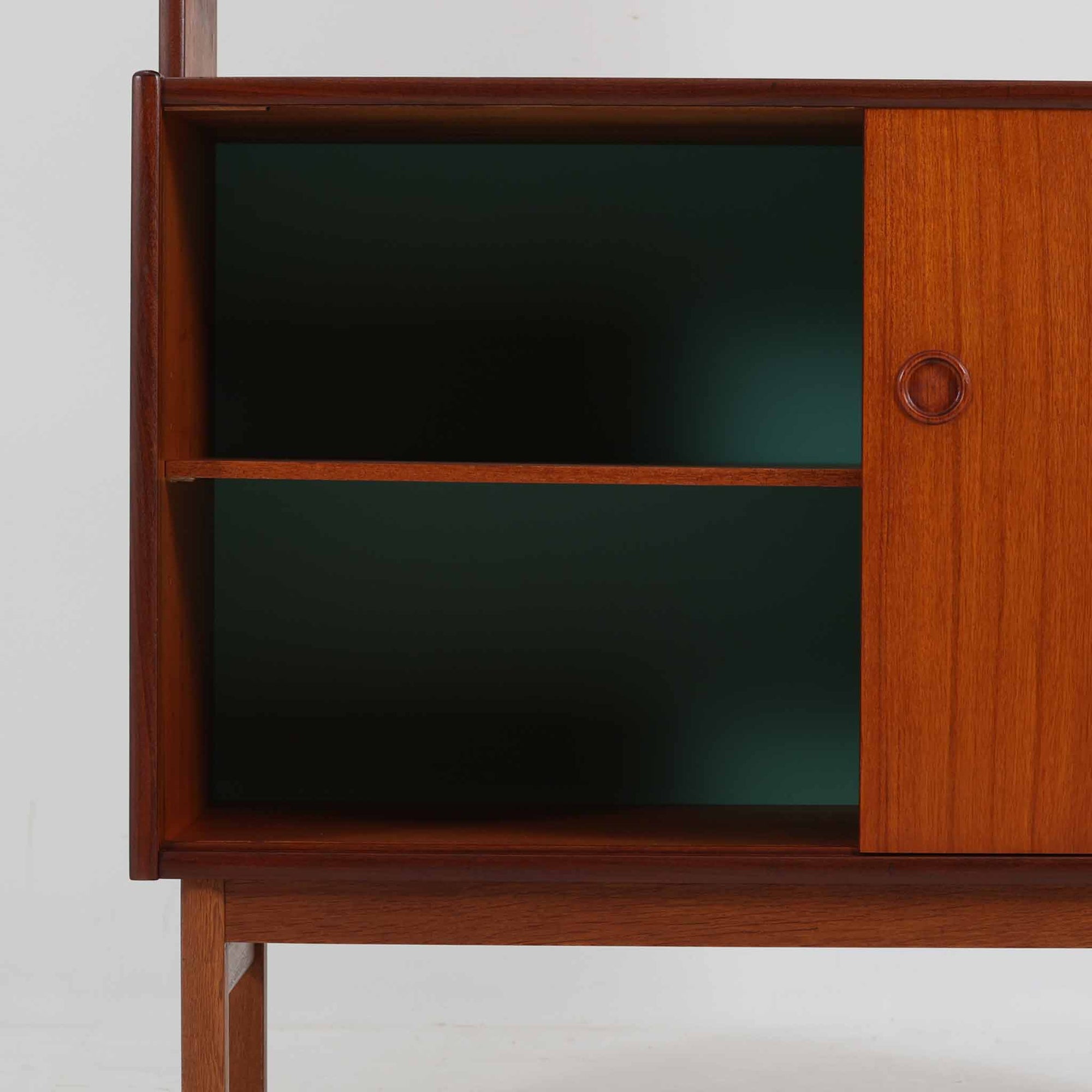 スウェーデン製のディスプレイシェルフです。上段には3段のオープンシェルフが設けられ、本や雑貨、オブジェなどを美しくディスプレイできます。下段にはスライド扉収納が備わり、内部の棚板によって整理しやすく、見せたくない収納にも便利です。チーク材の温もりある木目と、丸い掘り込み取っ手の柔らかなデザインが印象的で、北欧家具らしい穏やかな雰囲気を演出します。背面のグリーンの化粧板が空間に個性を添え、飾るアイテムをより際立たせます。本体にはチーク材、脚部にはオーク材が使用されており、素材のコントラストも魅力のひとつです。下段収納部の棚板にわずかな反りがありますが、裏返して使用することで目立たなくなります。軽やかな佇まいと実用性を兼ね備えた、北欧ビンテージらしい一台です。