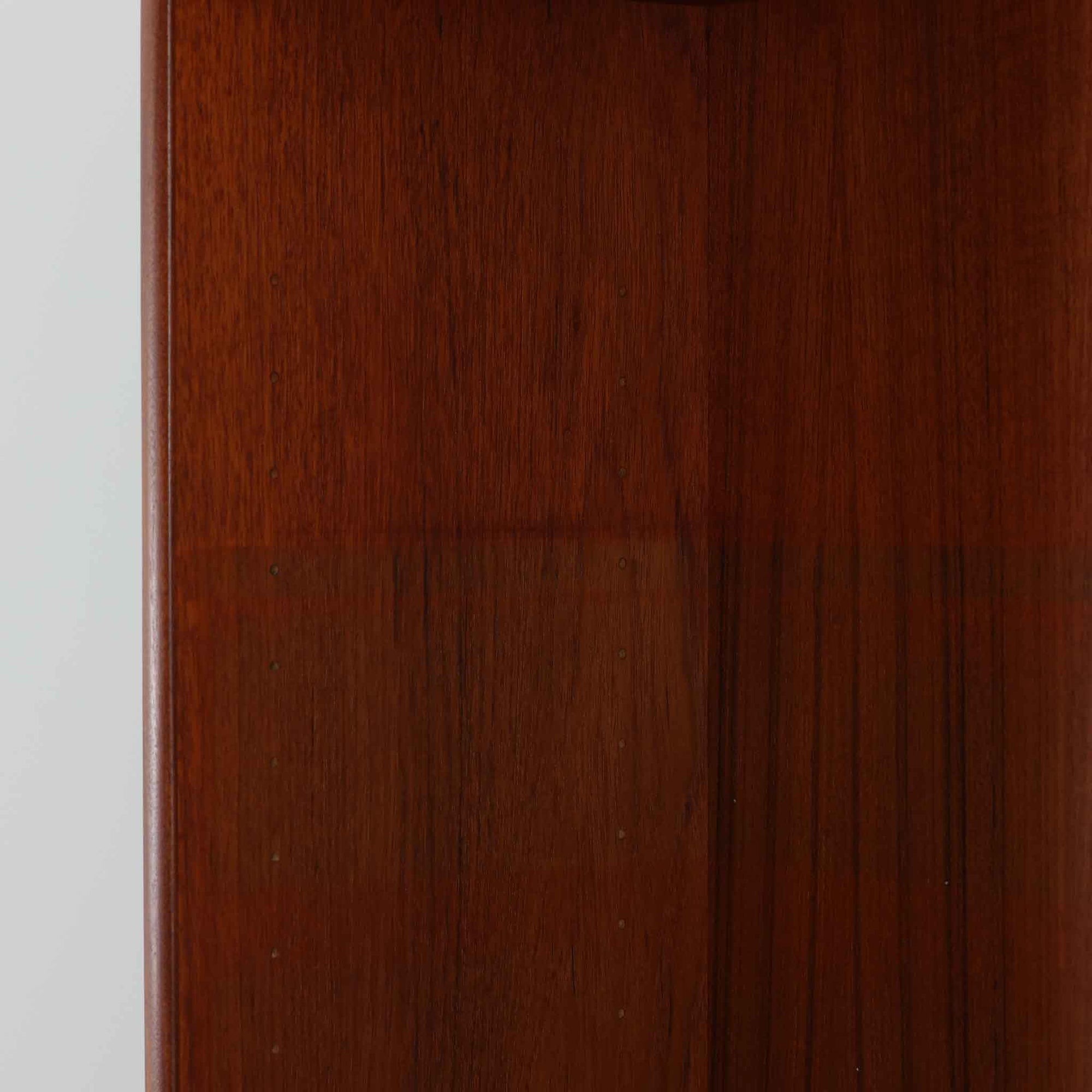 スウェーデン製のディスプレイシェルフです。上段には3段のオープンシェルフが設けられ、本や雑貨、オブジェなどを美しくディスプレイできます。下段にはスライド扉収納が備わり、内部の棚板によって整理しやすく、見せたくない収納にも便利です。チーク材の温もりある木目と、丸い掘り込み取っ手の柔らかなデザインが印象的で、北欧家具らしい穏やかな雰囲気を演出します。背面のグリーンの化粧板が空間に個性を添え、飾るアイテムをより際立たせます。本体にはチーク材、脚部にはオーク材が使用されており、素材のコントラストも魅力のひとつです。下段収納部の棚板にわずかな反りがありますが、裏返して使用することで目立たなくなります。軽やかな佇まいと実用性を兼ね備えた、北欧ビンテージらしい一台です。