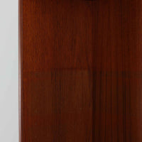 スウェーデン製のディスプレイシェルフです。上段には3段のオープンシェルフが設けられ、本や雑貨、オブジェなどを美しくディスプレイできます。下段にはスライド扉収納が備わり、内部の棚板によって整理しやすく、見せたくない収納にも便利です。チーク材の温もりある木目と、丸い掘り込み取っ手の柔らかなデザインが印象的で、北欧家具らしい穏やかな雰囲気を演出します。背面のグリーンの化粧板が空間に個性を添え、飾るアイテムをより際立たせます。本体にはチーク材、脚部にはオーク材が使用されており、素材のコントラストも魅力のひとつです。下段収納部の棚板にわずかな反りがありますが、裏返して使用することで目立たなくなります。軽やかな佇まいと実用性を兼ね備えた、北欧ビンテージらしい一台です。