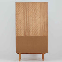 スウェーデン製のディスプレイシェルフです。上部は高さ調整可能な棚板が設けられており、書籍やオブジェの収納・展示に最適です。中央には小引き出しが2杯備わり、カトラリーや小物の整理にも便利。下部には扉付きの収納スペースがあり、日用品をすっきりと収納できます。素材にはチーク（本体）・オーク（脚の幕板）・ビーチ（脚）の3種の木材が用いられ、異なる木目のコントラストが美しい仕上がりです。北欧家具らしい温もりと実用性を兼ね備えた一台で、リビングやダイニング、書斎など幅広いシーンに調和します。