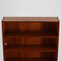 スウェーデン製のディスプレイシェルフです。上部は高さ調整可能な棚板が設けられており、書籍やオブジェの収納・展示に最適です。中央には小引き出しが2杯備わり、カトラリーや小物の整理にも便利。下部には扉付きの収納スペースがあり、日用品をすっきりと収納できます。素材にはチーク（本体）・オーク（脚の幕板）・ビーチ（脚）の3種の木材が用いられ、異なる木目のコントラストが美しい仕上がりです。北欧家具らしい温もりと実用性を兼ね備えた一台で、リビングやダイニング、書斎など幅広いシーンに調和します。