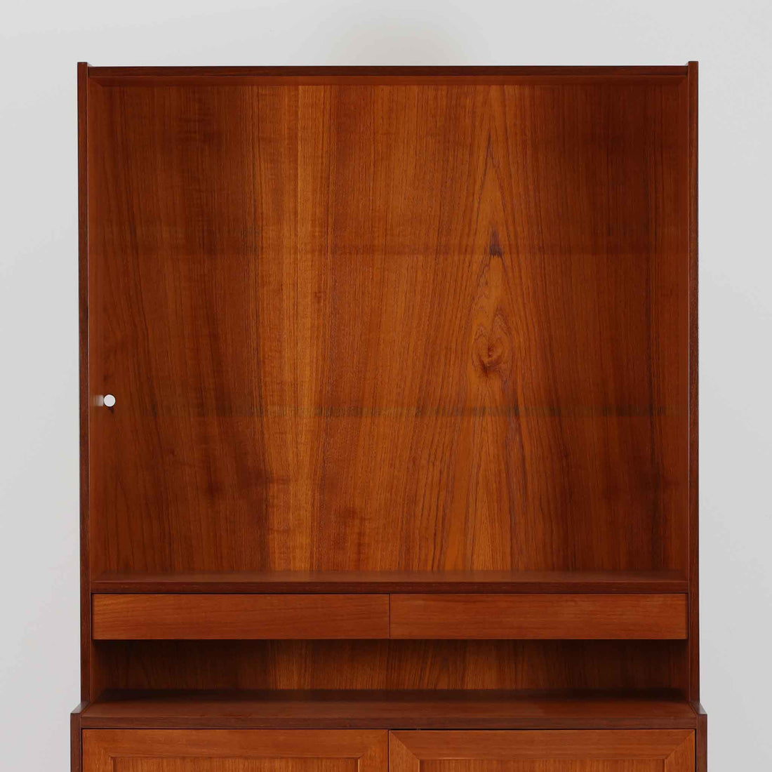 スウェーデン製のディスプレイシェルフです。上部は高さ調整可能な棚板が設けられており、書籍やオブジェの収納・展示に最適です。中央には小引き出しが2杯備わり、カトラリーや小物の整理にも便利。下部には扉付きの収納スペースがあり、日用品をすっきりと収納できます。素材にはチーク（本体）・オーク（脚の幕板）・ビーチ（脚）の3種の木材が用いられ、異なる木目のコントラストが美しい仕上がりです。北欧家具らしい温もりと実用性を兼ね備えた一台で、リビングやダイニング、書斎など幅広いシーンに調和します。