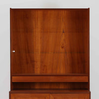 スウェーデン製のディスプレイシェルフです。上部は高さ調整可能な棚板が設けられており、書籍やオブジェの収納・展示に最適です。中央には小引き出しが2杯備わり、カトラリーや小物の整理にも便利。下部には扉付きの収納スペースがあり、日用品をすっきりと収納できます。素材にはチーク（本体）・オーク（脚の幕板）・ビーチ（脚）の3種の木材が用いられ、異なる木目のコントラストが美しい仕上がりです。北欧家具らしい温もりと実用性を兼ね備えた一台で、リビングやダイニング、書斎など幅広いシーンに調和します。