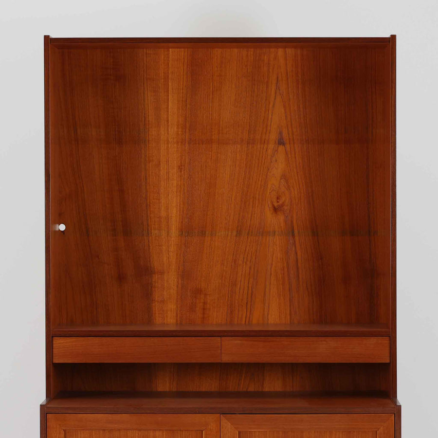 スウェーデン製のディスプレイシェルフです。上部は高さ調整可能な棚板が設けられており、書籍やオブジェの収納・展示に最適です。中央には小引き出しが2杯備わり、カトラリーや小物の整理にも便利。下部には扉付きの収納スペースがあり、日用品をすっきりと収納できます。素材にはチーク（本体）・オーク（脚の幕板）・ビーチ（脚）の3種の木材が用いられ、異なる木目のコントラストが美しい仕上がりです。北欧家具らしい温もりと実用性を兼ね備えた一台で、リビングやダイニング、書斎など幅広いシーンに調和します。